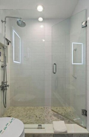 A glass-enclosed shower with a handheld showerhead, a glass door, and a small bench with a towel. - CondoPool/StepsToBeachDine/Getaway2br (Palm Beach)