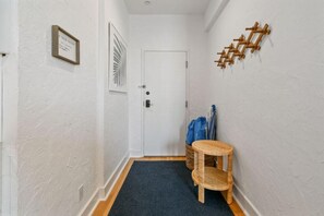 A narrow hallway with a door, a framed picture, a small wicker table, and a wall-mounted rack.