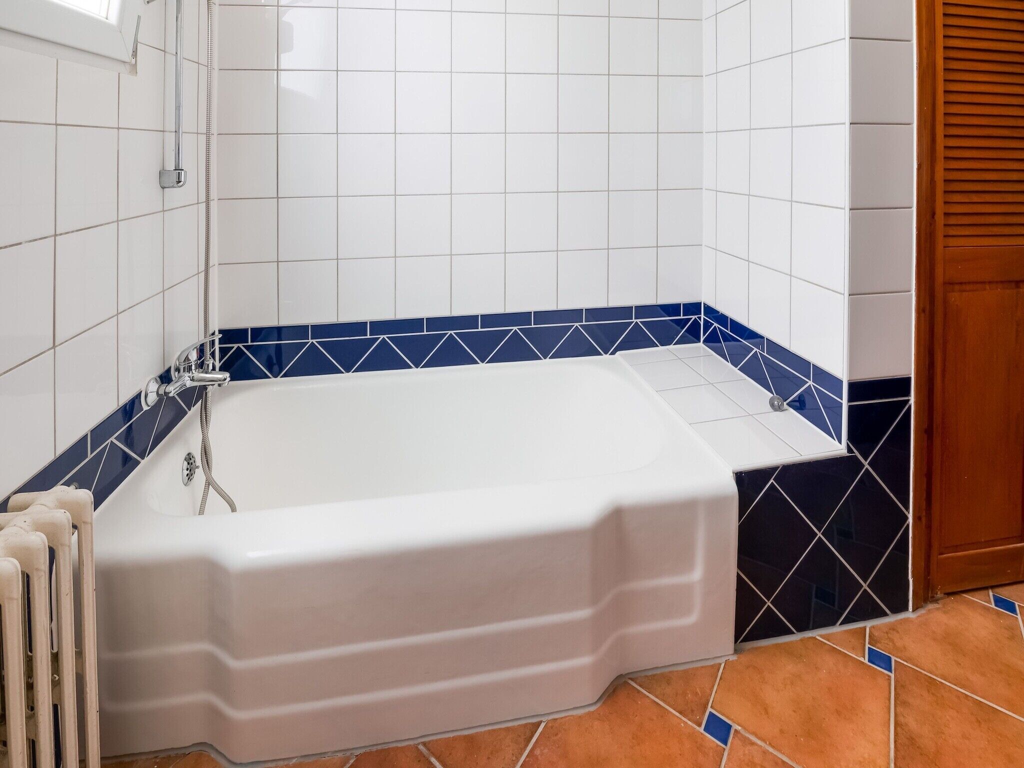 Casa de banho com banheira branca, zona de duche revestida a azulejos azuis e porta de madeira.