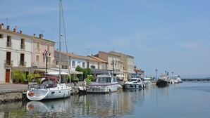 Un port de plaisance où plusieurs bateaux sont amarrés le long d’une promenade, avec des bâtiments en arrière-plan.