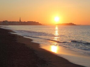 Ein Strand mit Sonnenuntergang, Wellen und einer entfernten Skyline.
