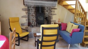 Ein gemütliches Wohnzimmer mit Kamin aus Stein, gelben Sesseln, einem blauen Sofa und einer Holztreppe.