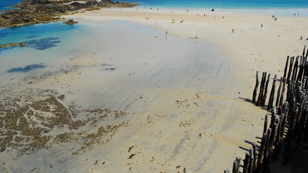 Ein Strand mit einer Felsformation und einem festungsähnlichen Bauwerk.