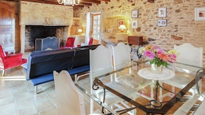 A rustic room with a stone wall, wooden ceiling beams, a fireplace, and a glass table with chairs.