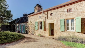 A stone building with green shutters, a gravel path, and a small garden.