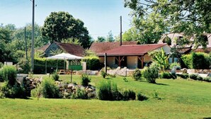 Una casa de techo rojo, rodeada de un césped cuidado y diversas plantas.