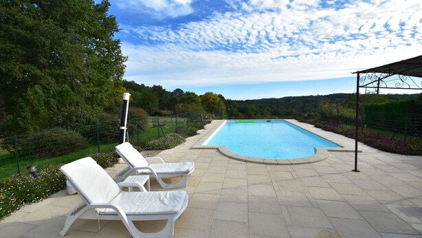 Una piscina con dos sillones blancos y una pérgola.