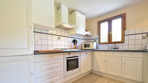Una cocina con armarios blancos, un microondas, un horno y una ventana con persianas.