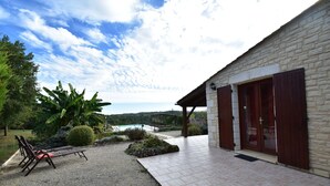 Un edificio moderno con fachada de piedra, un patio cubierto y vista a un cuerpo de agua al fondo.