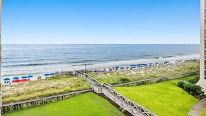 A beach view with a wooden boardwalk, beach umbrellas, and a grassy area. - Beautiful OCEAN VIEW! 2 FREE Beach chairs and umbrella! (Destin)