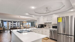 A modern kitchen with white cabinetry, a large island, stainless steel appliances, and a view to the living area. - Beautiful OCEAN VIEW! 2 FREE Beach chairs and umbrella! (Destin)