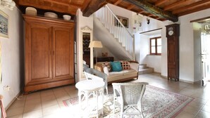 A spacious living area with a wooden ceiling, a staircase, a sofa, a dining table, and wicker furniture. - Saint-Sauveur Hideaway (St Sauveur Lendelin)