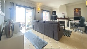 Un salon moderne avec un canapé gris, un téléviseur à écran plat, une cheminée et un coin repas comprenant une table et des chaises.