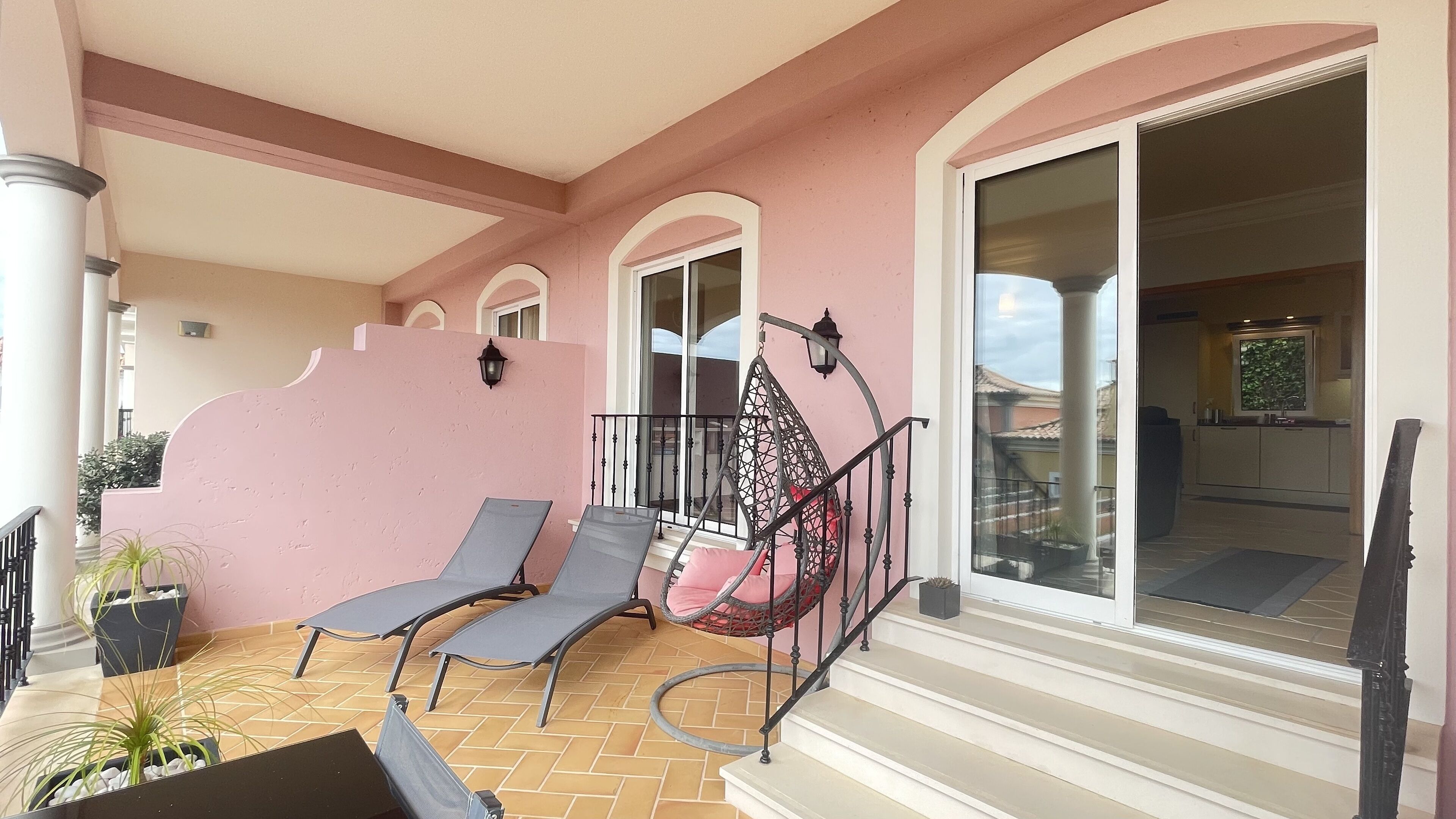 A balcony with two lounge chairs, a decorative wall, and a staircase leading to an upper level.