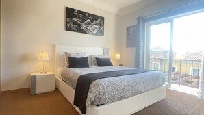 Une chambre d’hôtel avec un grand lit, deux tables de chevet avec des lampes, un tableau au mur et un balcon avec vue.