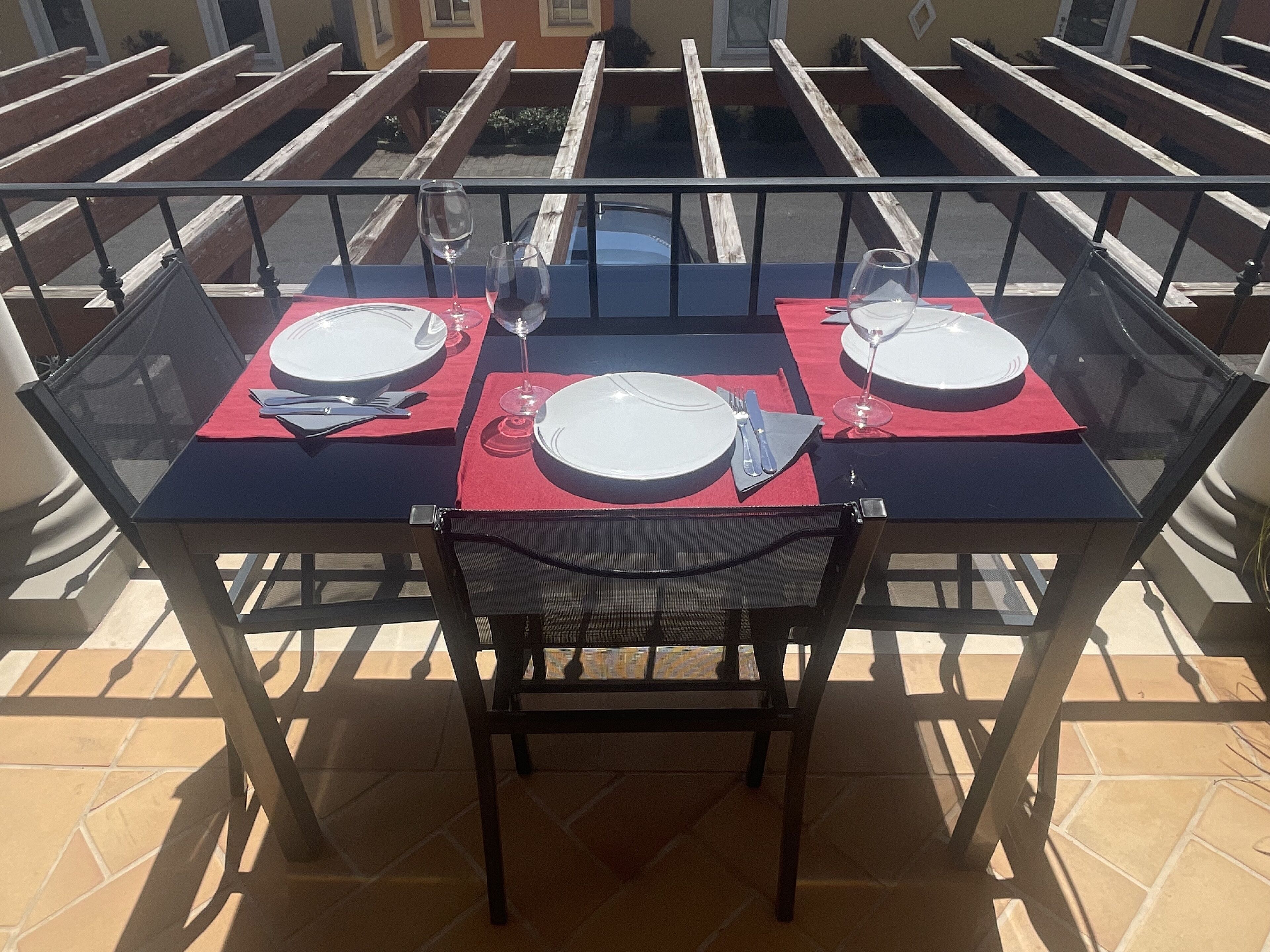 A glass-top table set for two with red placemats, white plates, and cutlery.