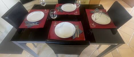 A dining table set for four with red placemats, white plates, and cutlery.