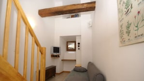 Un escalier avec des rampes en bois mène à un espace de vie comprenant un canapé et un téléviseur posé sur une étagère.