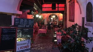 Un espace de restauration en plein air avec des tables et des chaises, un tableau noir affichant le menu et une enseigne indiquant « Restaurant L’Écurie ».