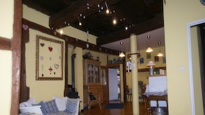 Un salon chaleureux avec un canapé, des poutres en bois, une cheminée et des luminaires suspendus.