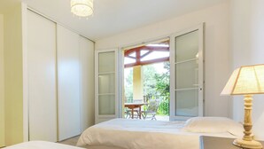 A bedroom with two beds, a desk, and a balcony with a table and chairs.