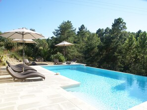 A swimming pool with lounge chairs and umbrellas, surrounded by trees.