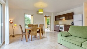 A modern kitchen with dark wooden cabinets, a white refrigerator, and a dining area with wicker chairs and a table.