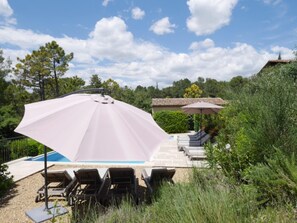 A poolside area with lounge chairs, a large umbrella, and a building with a tiled roof.
