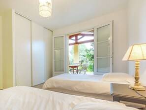 A bedroom with two beds, a table with chairs, and a balcony with a table and chairs.