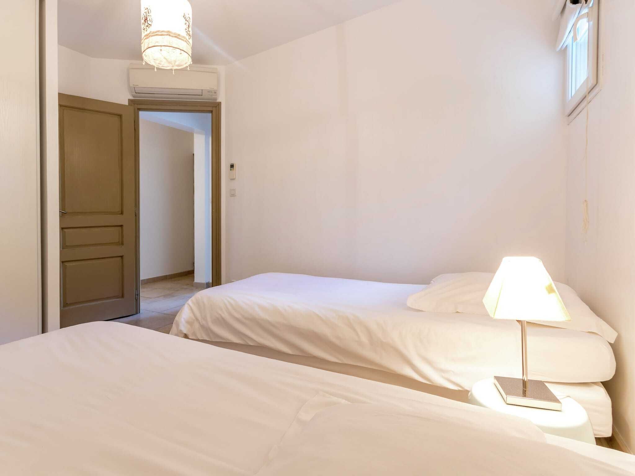 Hotellihuone, jossa on kaksi sänkyä, yöpöytälamppu ja ovi, joka johtaa toiseen huoneeseen.
