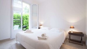 A bedroom with a large bed, two bedside lamps, a nightstand, and a view of greenery outside. - Apartment in Montauroux with Pool & Forest Views (Montauroux)
