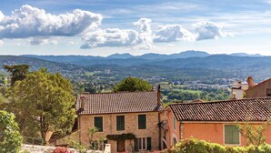 A stone building with a tiled roof, surrounded by greenery and mountains in the background. - Apartment in Montauroux with Pool & Forest Views (Montauroux)