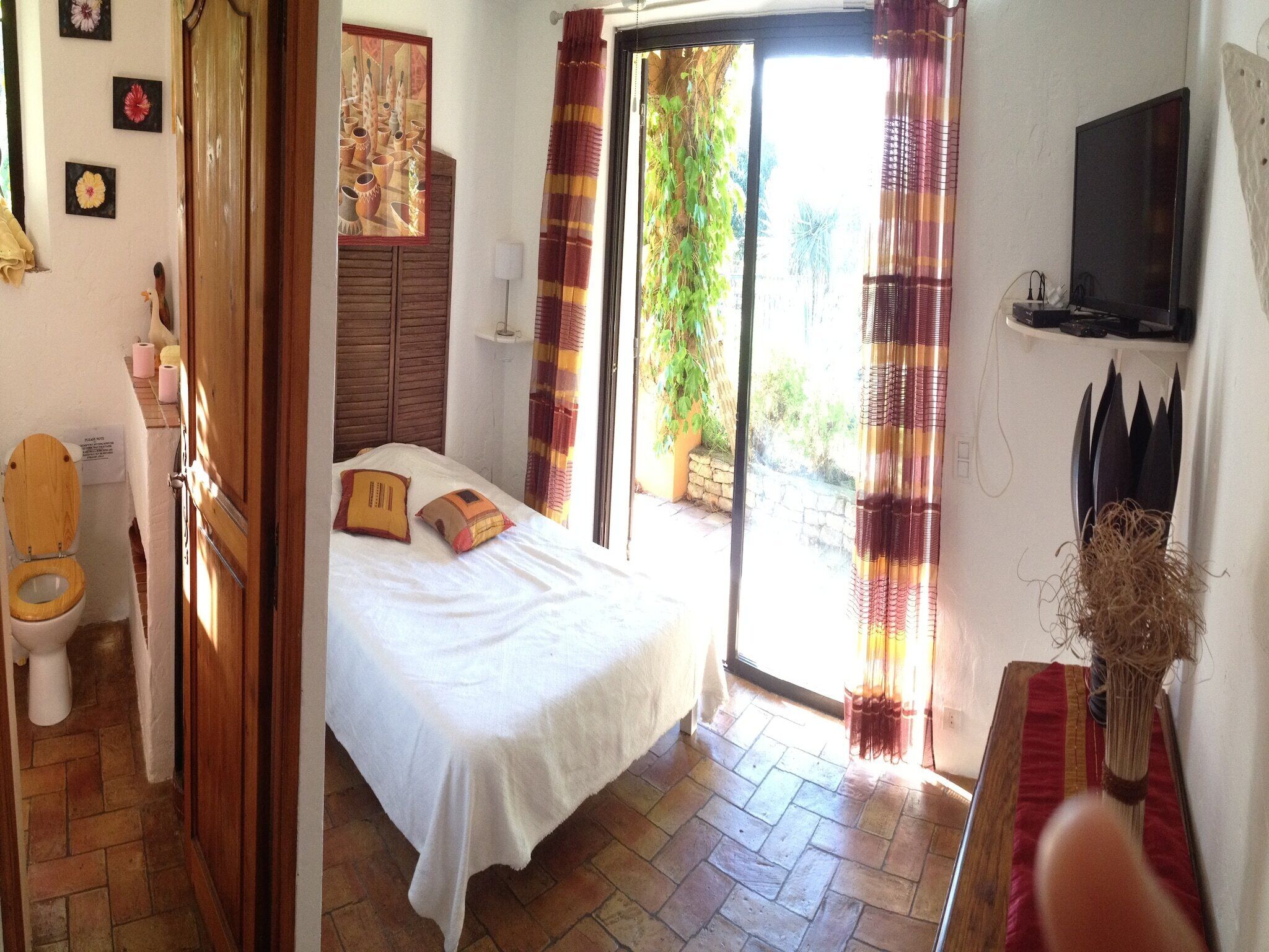 A bedroom with a bed, a wooden door, a toilet, and a television on the wall.