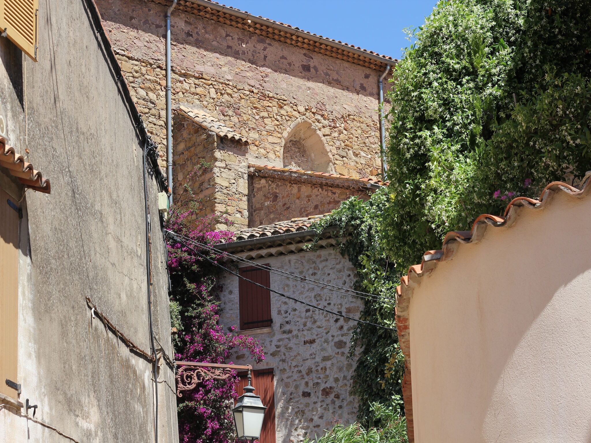 A narrow street with a stone building featuring a tiled roof and a small arched window.