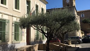 A building with a clock tower, a tree in front, and parked cars. - Holiday Home in Piolenc near Roman Orange (Piolenc)