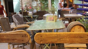Un espace extérieur aménagé avec des chaises en osier et un banc en bois, entouré de tables et de plantes en pot.