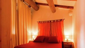 Une chambre à coucher avec un lit, des rideaux, deux tables de chevet avec des lampes et une poutre en bois au plafond.