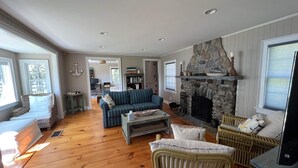 Een ruime woonkamer met een stenen openhaard, houten vloeren en een groot raam.