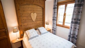 A bedroom with a wooden headboard, a bed with patterned bedding, bedside lamps, and curtains with a deer and heart pattern. - Chalet in Ventron near Ski Lift (Ventron)