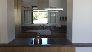Una cocina moderna con armarios de madera, un hervidor de acero inoxidable, un lavabo y una ventana con vistas a zonas verdes.