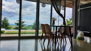 Un'area pranzo con tavolo e sedie, ampie finestre che offrono vista su vegetazione ed edifici, e un lampadario.