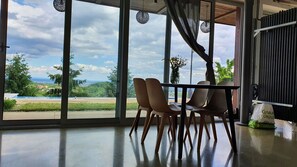 A dining area with a table and chairs, large windows with a view of greenery and buildings, and a hanging light fixture. - VILLA WITH PRIVATE POOL (Zagreb)