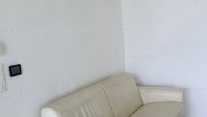 Un divano in pelle bianca in un angolo della stanza, con un tavolino in legno e un cestino dei rifiuti verde.