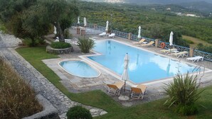 Une piscine entourée de chaises longues et de parasols, avec une végétation luxuriante et des montagnes en toile de fond.