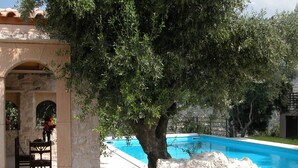 A stone pool with a tree in the foreground, a stone archway, and a chair. - Villa Despoina in Malades (Malades)