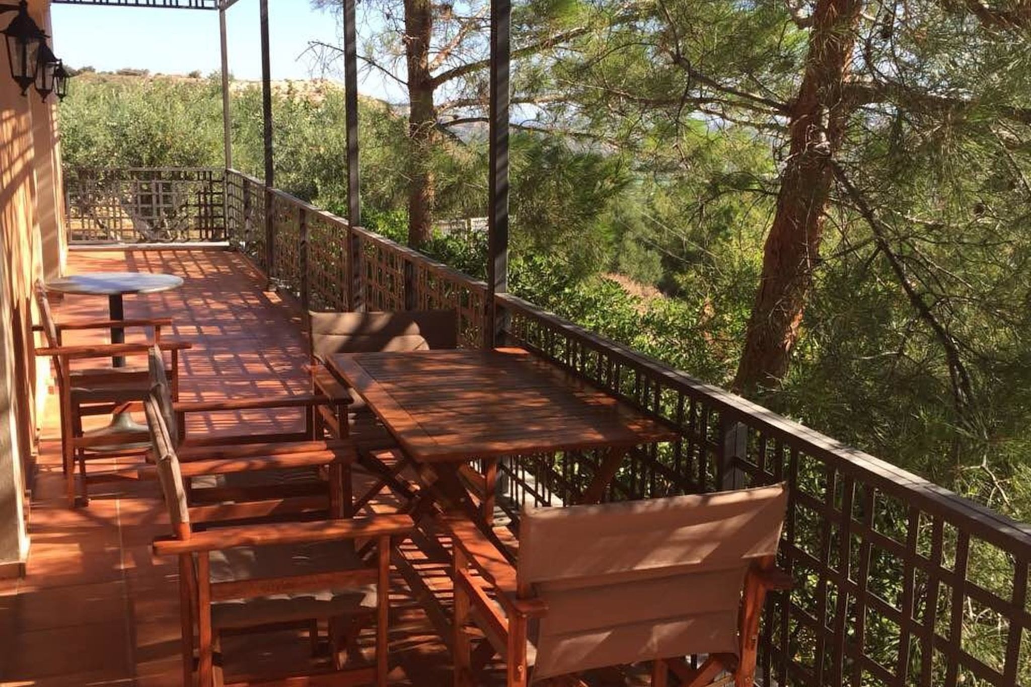 Une terrasse en bois, agrémentée de tables et de chaises, entourée d’une rambarde en métal, et offrant une vue sur une forêt dense.