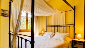 A four-poster bed with white linens, a nightstand with a lamp, and a view of greenery outside. - Villa Despoina in Malades (Malades)