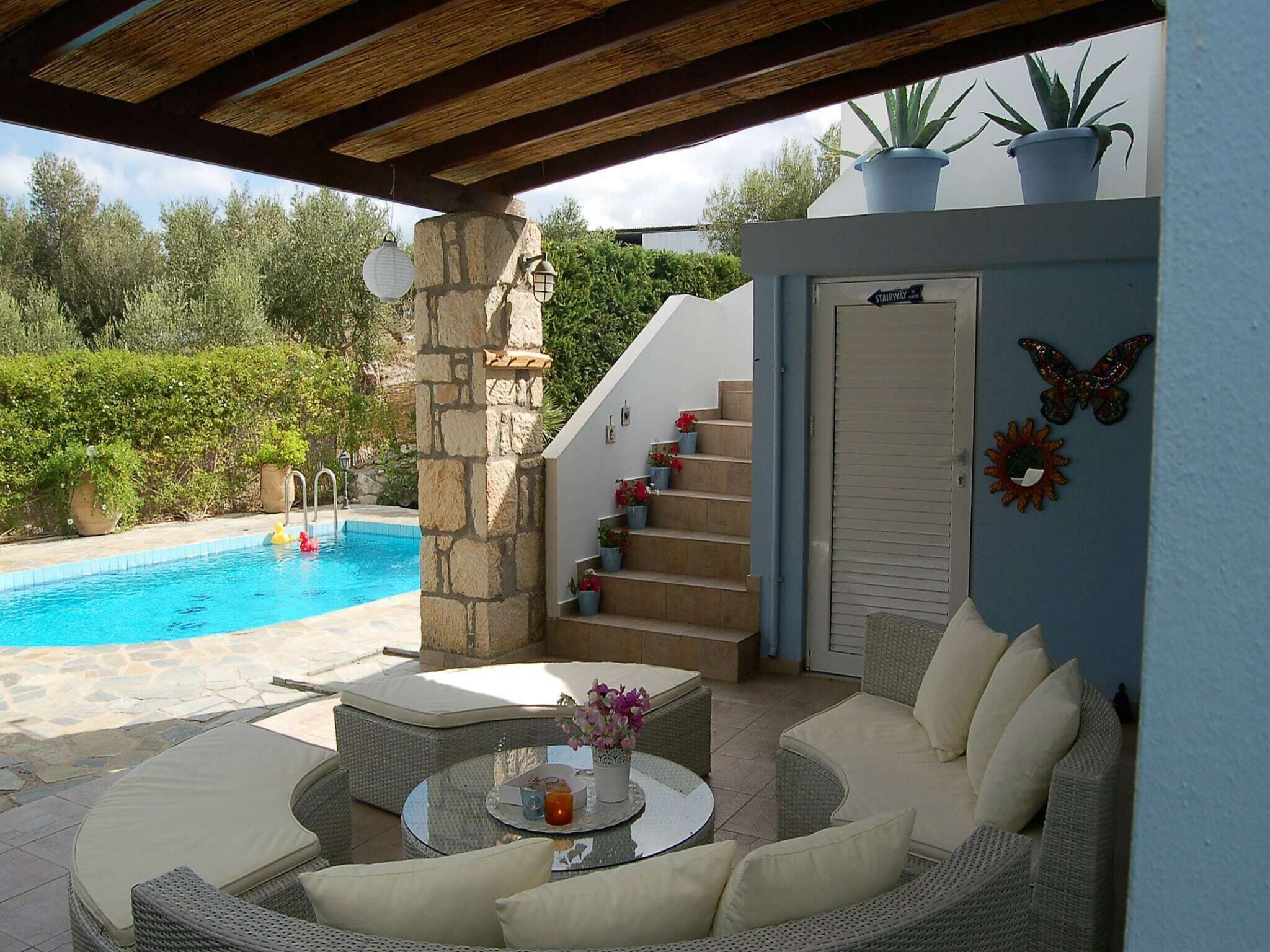 A covered outdoor area with a pool, wicker furniture, and a stone pillar.