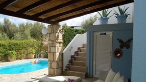 A covered outdoor area with a pool, wicker furniture, and a stone pillar.