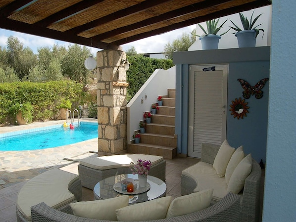 A covered outdoor area with a pool, wicker furniture, and a stone pillar.